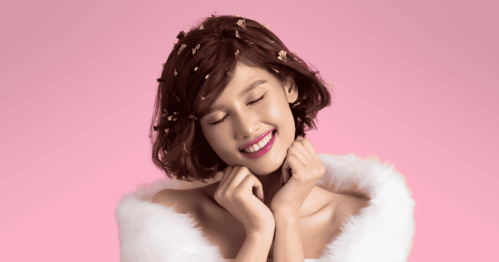 A smiling woman with short brown hair decorated with flower petals poses against a pink background, reflecting the theme of why narcissists target attractive people and how to reclaim personal starlight.