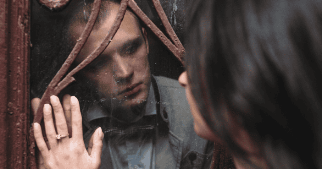 A man looks through a broken window while a woman’s hand touches the glass, reflecting the theme of why narcissists cheat and why it’s darker than you think.