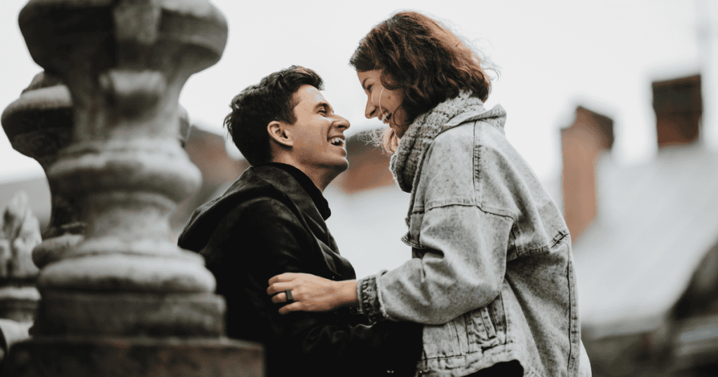 A joyful couple leans in close to share a laugh, reflecting the quiet security of having someone show up for you steadily.