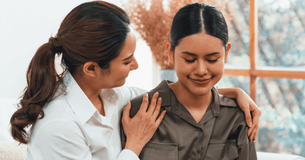 One woman places a comforting hand on the shoulder of another who is looking down, illustrating a deep-seated drive to mend someone else's pain.