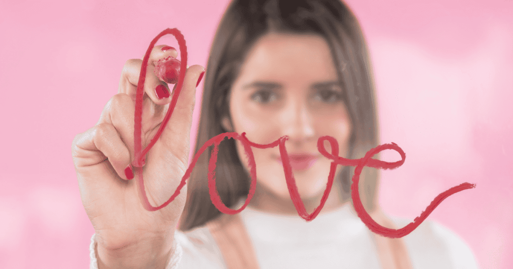 A woman writes the word "love" on a glass surface with red lipstick, visually marking the pivotal step of reconnecting with her physical self.