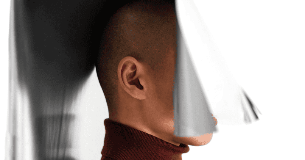 A profile view of a man’s head partially obscured by a heavy, metallic-colored shroud, representing the progressive loss of self during a dark transformation.