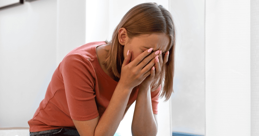 A woman sits with her face buried in her hands; the isolation of the shot highlights the vulnerability that can be used as a target for ridicule.