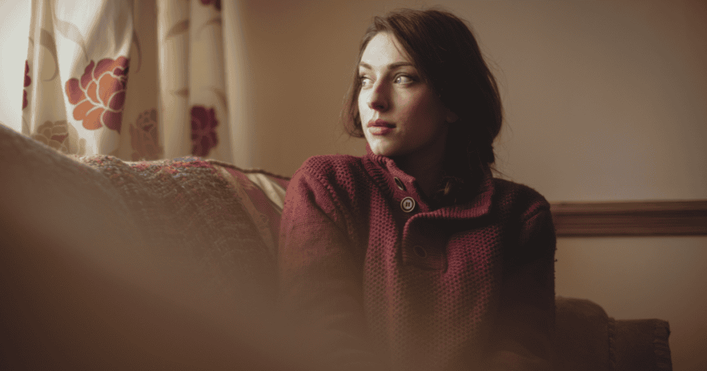 A woman in a burgundy sweater gazes thoughtfully out a window; her calm posture suggests a newfound sense of personal space.