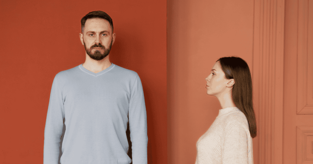 A man and a woman stand side-by-side but look in opposite directions; the physical gap reflects a shift in how they perceive one another.