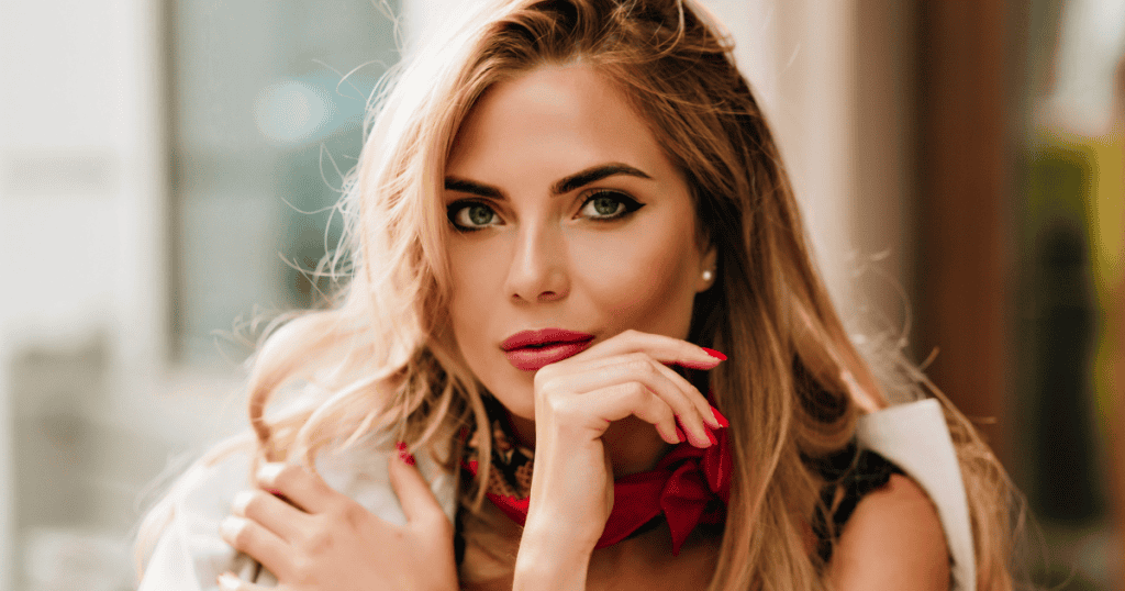 A blonde woman in a red neckerchief gazes intensely into the camera, her steady expression suggesting she has reclaimed her perspective and moved beyond a predetermined script.