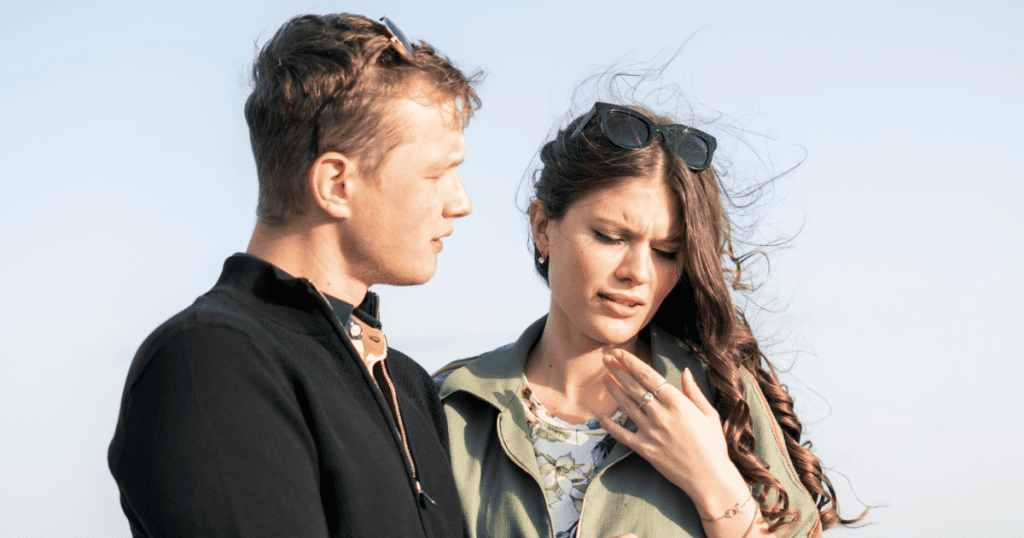 A woman winces and touches her chest while a man speaks closely to her, depicting how words can become a source of renewed agitation.