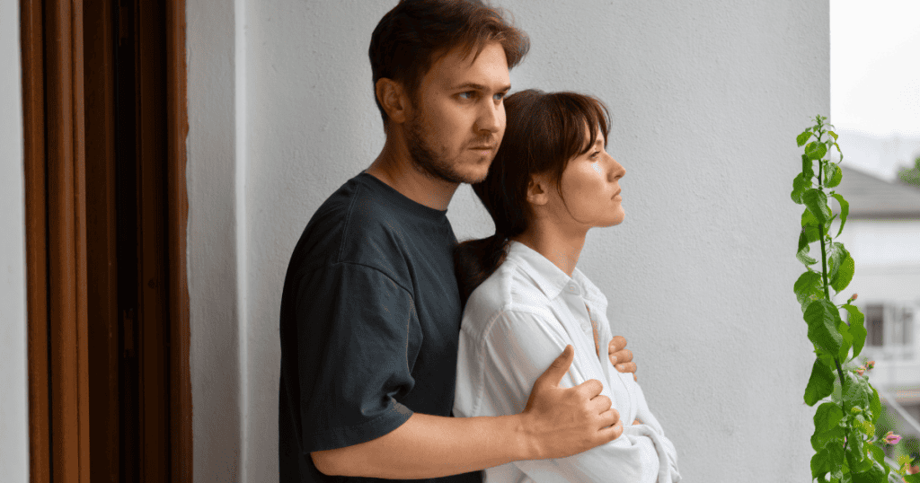 A man and woman stand close together while staring off in the same direction, reflecting a shared gaze that masks their internal, solitary realizations.
