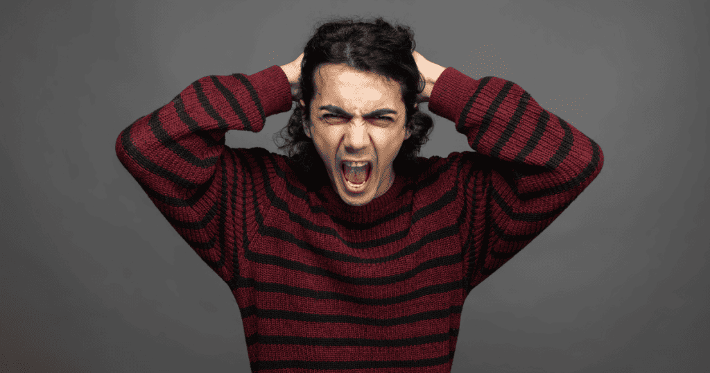 A man in a striped sweater grips his hair and screams in frustration, illustrating a volatile response to being challenged.