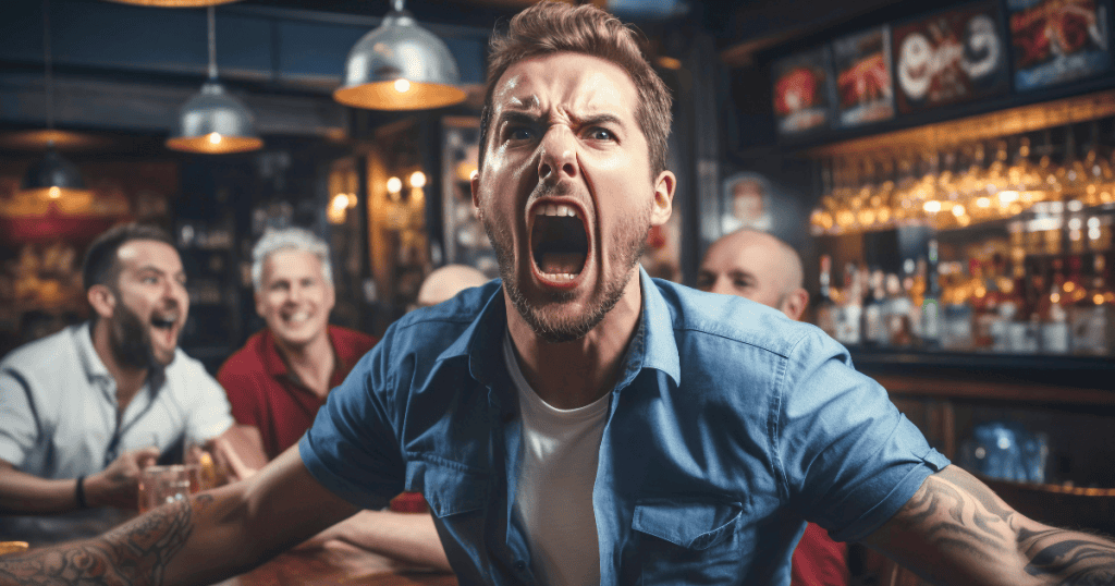 A man at a crowded bar leans forward with an aggressive, wide-mouthed shout, demonstrating a public display of defensive hostility.