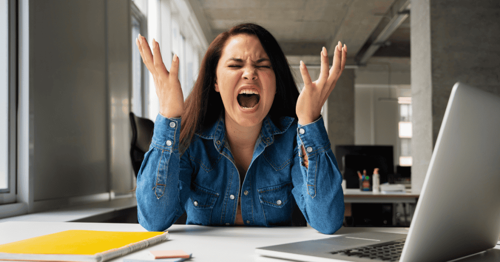 A woman sits at a desk with her hands raised in a frantic gesture of outrage, exposing the underlying truth behind a sudden emotional outburst.