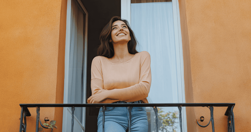 A woman smiling calmly on a balcony in warm sunlight, reflecting the quiet shift into a version of yourself they no longer recognize or influence