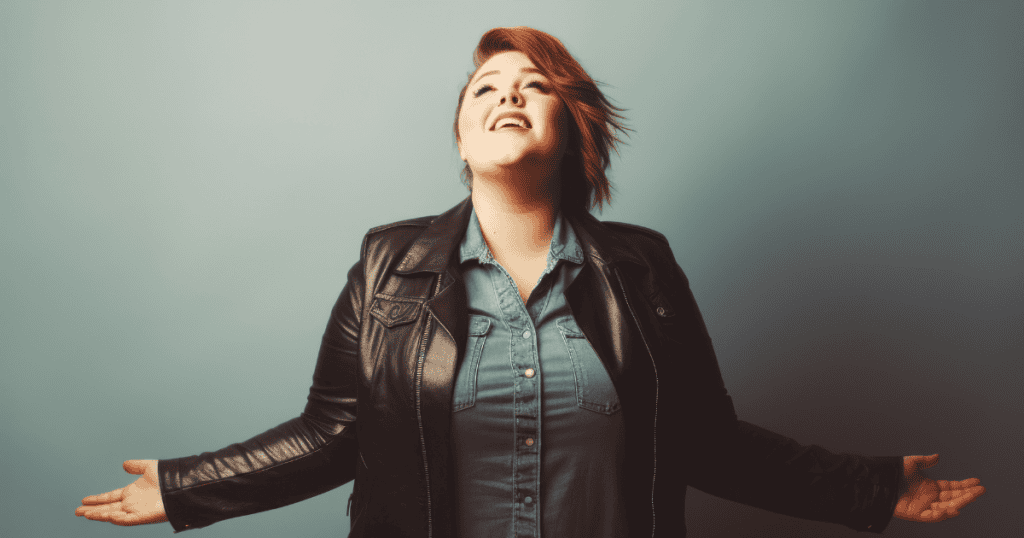 A woman in a leather jacket tilts her head back with open arms, projecting an air of elevated self-importance that places her above the rest.