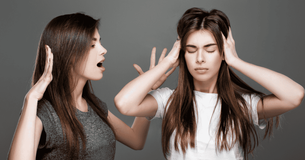A woman shouts at her companion who has her hands over her ears, a scene where a refusal to listen meets a direct deflection of responsibility.