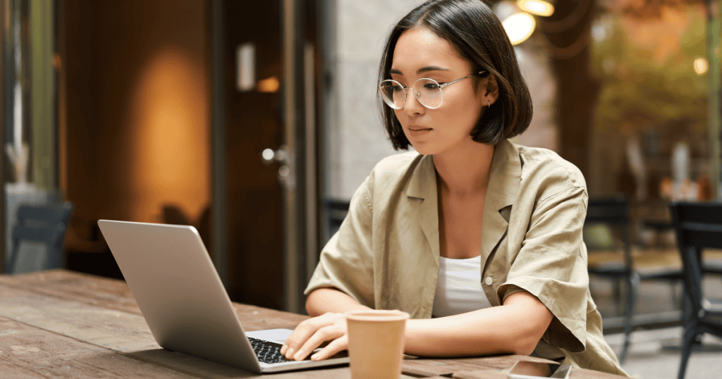 A focused woman works on her laptop at an outdoor cafe, her quiet isolation suggesting the stinging weight of being overlooked.