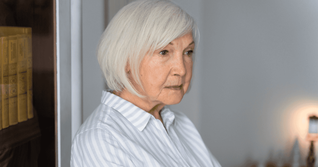 An elderly woman gazes off into the distance with a somber expression, her detached focus suggesting a profound emotional disconnect from her surroundings.