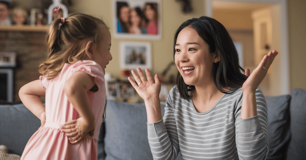 A woman and a young girl laugh together with their hands raised in excitement, showcasing the vital importance of maintaining a joyful, consistent emotional bond.