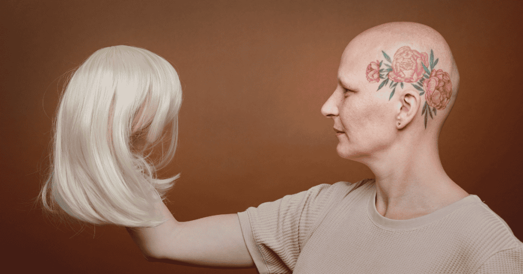A woman with a floral head tattoo looks at a blonde wig she is holding, representing a search for a persona to mask an underlying fragility in identity.