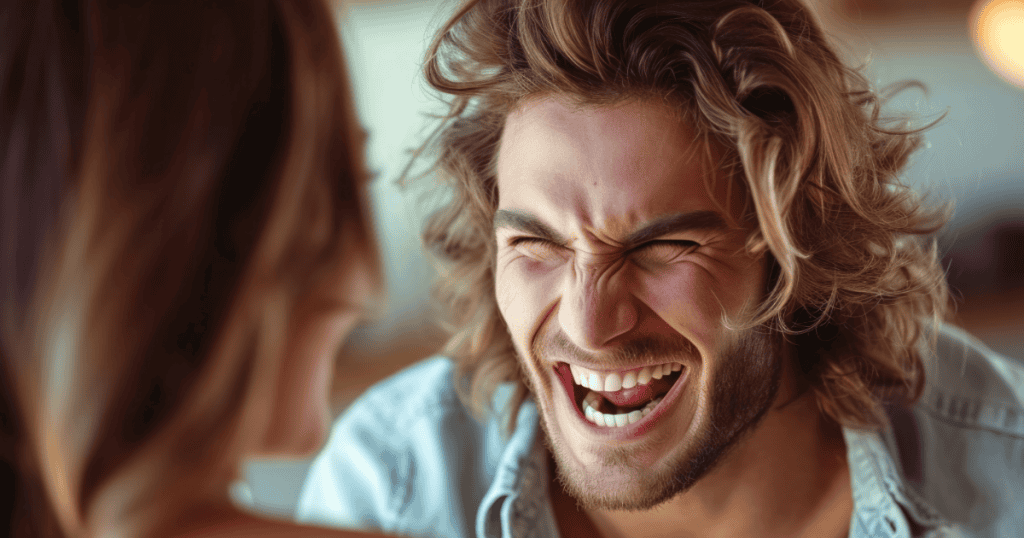 A man laughs with intense, exaggerated energy toward a woman, his overwhelming presence beginning to crowd out the space for her own happiness.