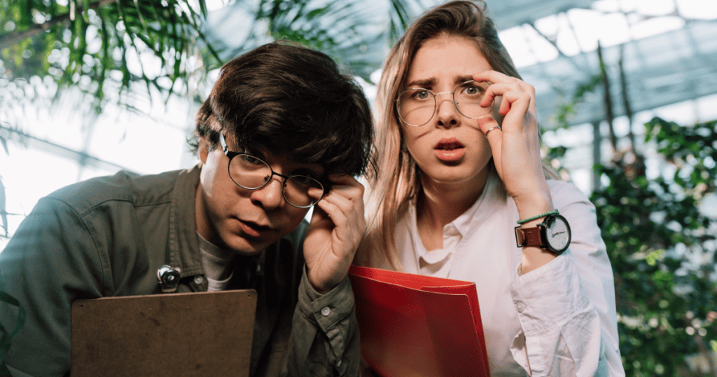 Two people look intently through glasses at something off-camera, depicting the curious and hyper-vigilant scrutiny used to assess others in real-time.