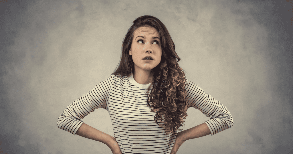 A young woman stands with hands on her hips and an inquisitive look, contemplating the past vulnerabilities that once clouded her judgment.