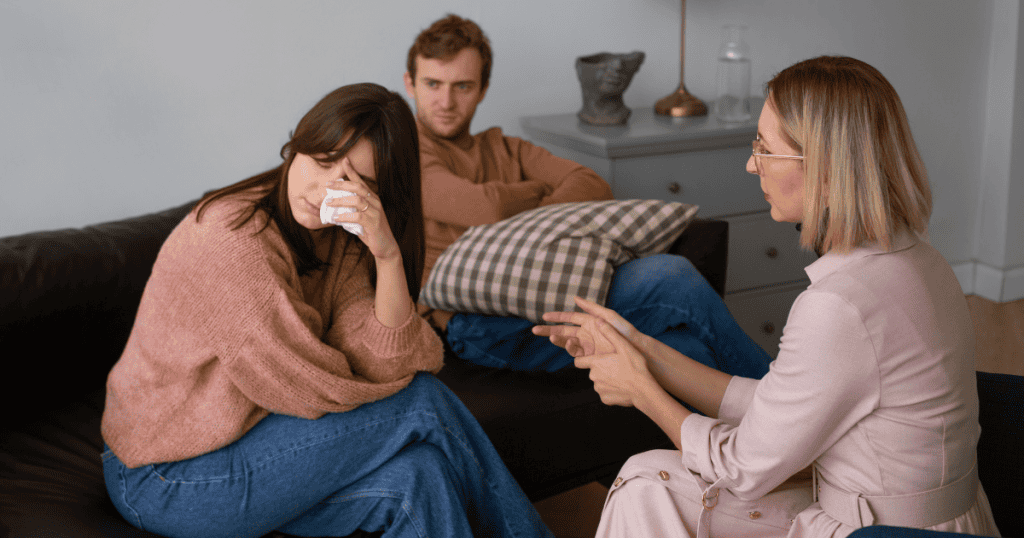 A woman wipes away tears during a tense group session, capturing the emotional weight of remaining within a distressing cycle.