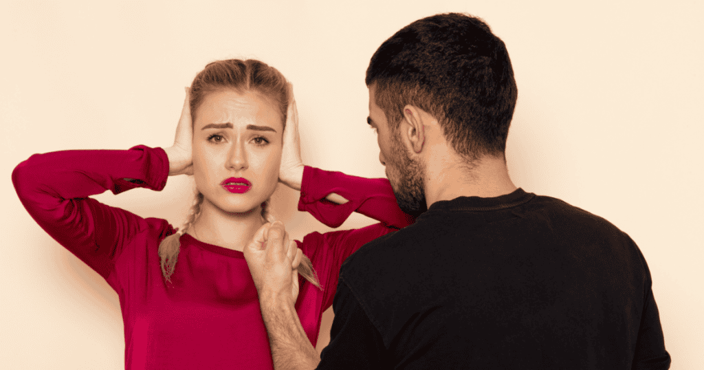 A man aggressively confronts a woman who is covering her ears, portraying the sudden transition from psychological hold to overt, shocking intimidation.