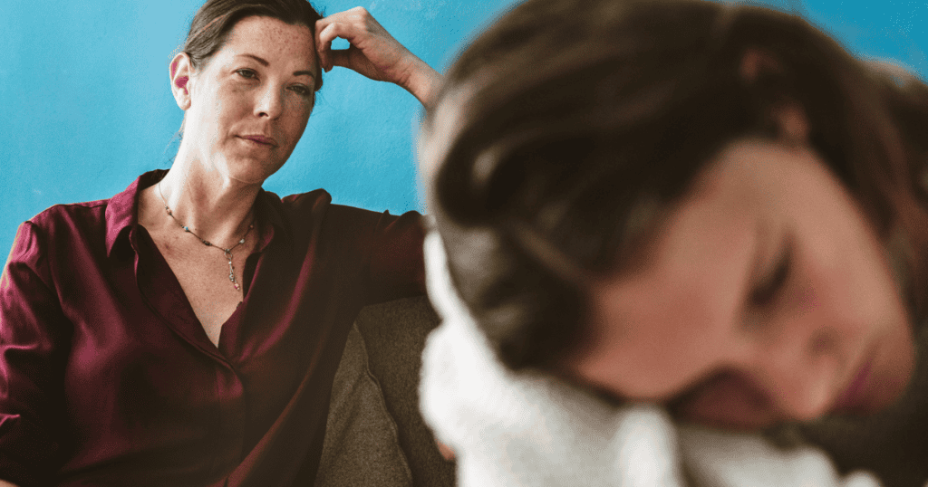 A woman watches a sleeping person with a heavy, contemplative gaze, suggesting the quiet vigilance of someone whose natural empathy makes them a seamless fit for another's needs.