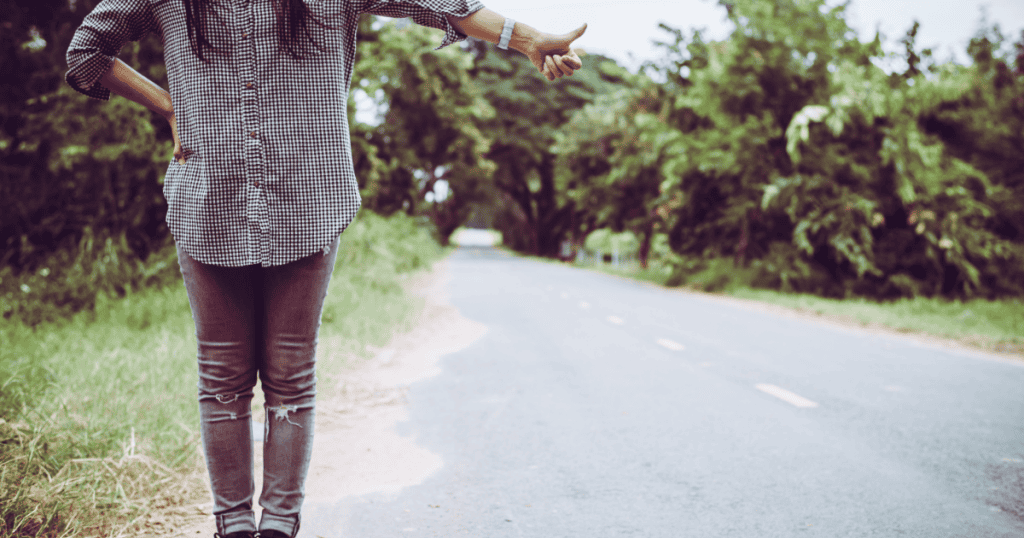 A person stands on the side of a road with their thumb out, embodying the quiet resolve of choosing a new path regardless of a formal explanation.