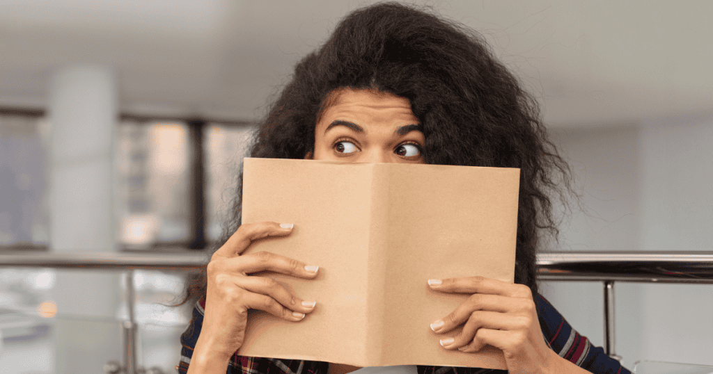 A woman peeks over the edge of a brown notebook with wide, darting eyes, as if she is navigating a world where the most important pieces are kept out of sight.