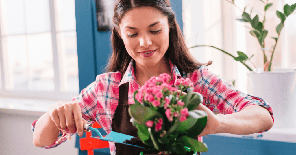 A woman smiles while carefully tending to a potted plant with a small shovel, her focus entirely consumed by a task that seems to require constant, meticulous adjustment.