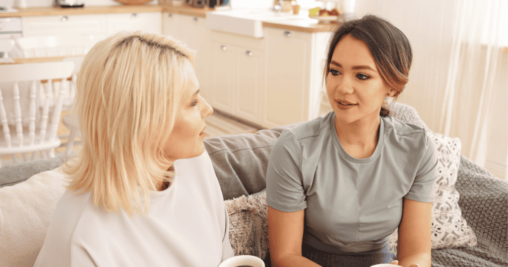 Two women sit closely on a couch engaged in calm conversation, suggesting a path toward mutual clarity that remains just out of reach.