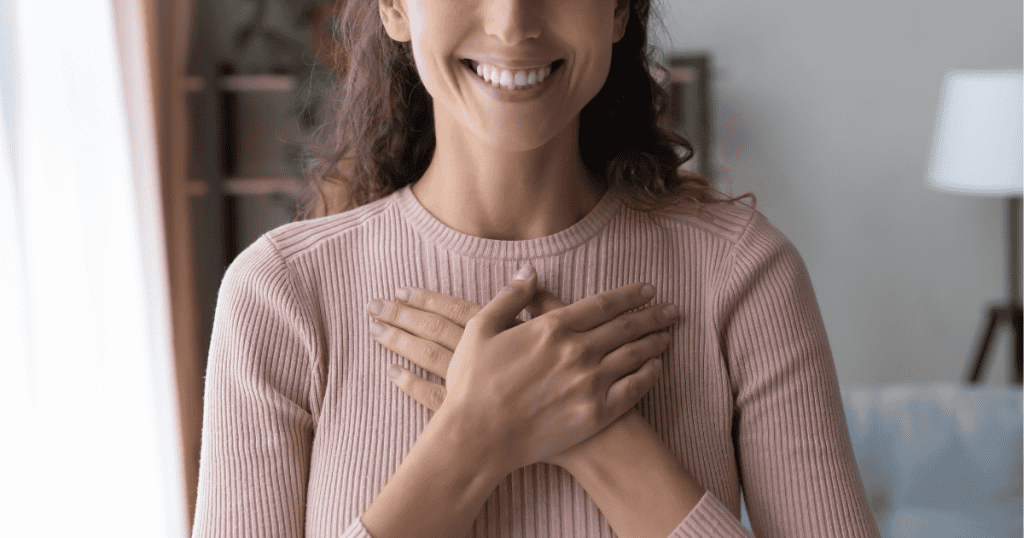A woman smiles warmly while pressing both hands to her chest in a gesture of sincerity, representing an idealized image of compassion that may mask a more complex motivation.