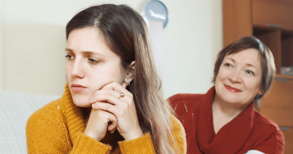 A young woman sits with a somber, guarded expression while an older woman smiles pleasantly behind her, illustrating the tension between an outward display of warmth and an inner need for distance.