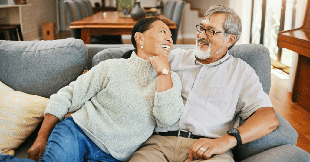 An older couple shares a cozy laugh on a sofa, portraying the polished exterior of a union used as a social credential.