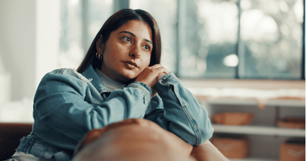 A woman leans forward with her chin resting heavily on her hands while gazing out a window, reflecting the internal paralysis that prolongs a stay in an unhealthy environment.