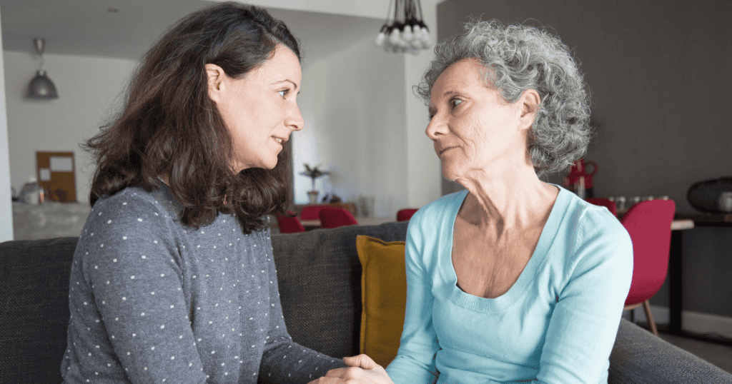 An older woman and a younger woman sit closely together holding hands while looking intensely at one another, showcasing the deep emotional entanglement that often precedes a sharp transition.