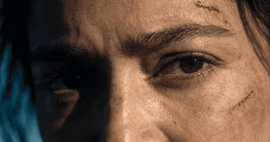 A harsh, dramatic close-up of a person's eyes reveals a small laceration on their forehead, highlighting a realistic and unvarnished acknowledgment of personal vulnerability and battle scars.