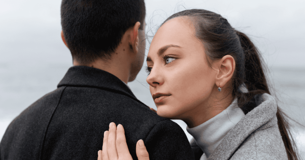 A woman rests her head gently against a man's shoulder from behind while looking off to the side with an analytical gaze, reflecting a deep emotional investment that is quietly being reconsidered.