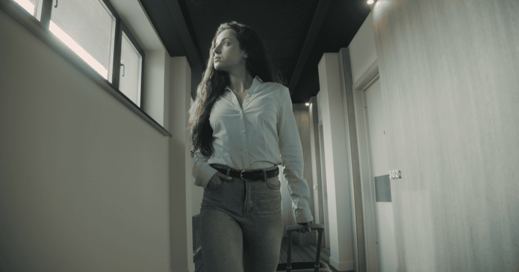 A young woman glances out a window while pulling a rolling suitcase down a long hallway, showcasing the quiet power of choosing physical relocation over endless debate.