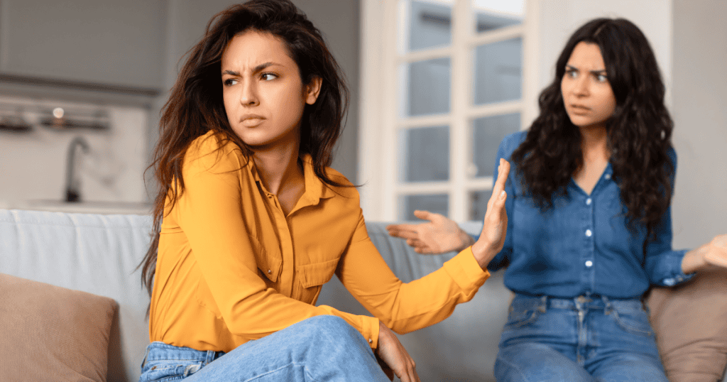 A woman in a yellow shirt looks away with a sharp, dismissive hand gesture toward another woman, portraying the blunt and unsympathetic nature of a final rejection.