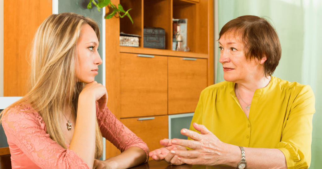Two women sit at a table while the older one speaks and the younger one looks away, showing a clear failure to connect during a hard line.
