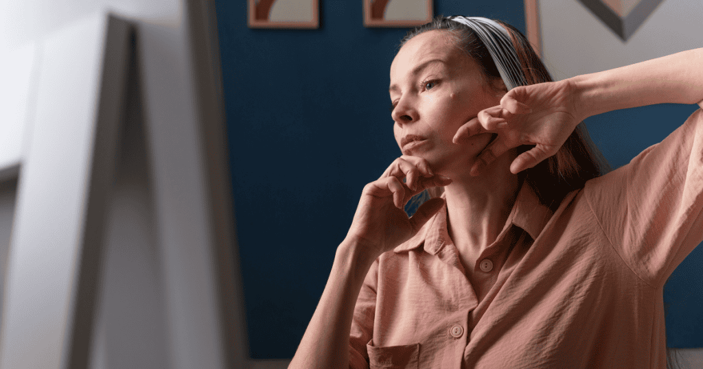A woman rests her chin on her hand and stares blankly into the distance with a pensive look, capturing the deep internal questioning that occurs when one's worth has been tied to another's approval.