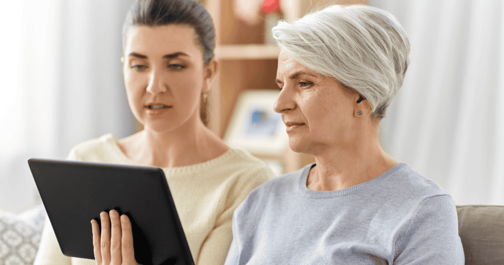 An older woman and a younger woman sit side-by-side reviewing content together on a tablet screen, highlighting a shared focus that can mask a deeper, persistent attachment.