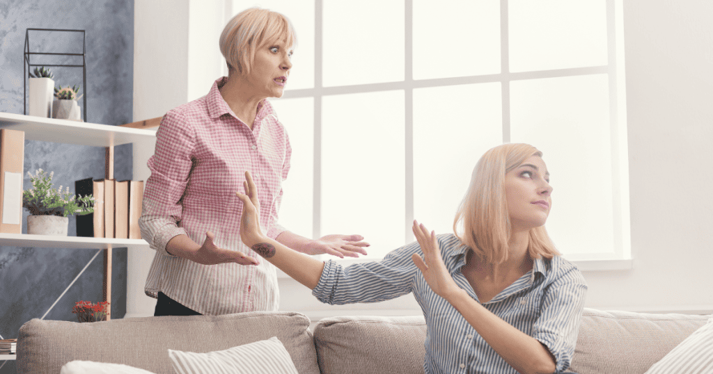 A younger woman looks away and raises her hands in a dismissive gesture while an older woman speaks intensely to her, marking the definitive release of a burden that was never hers to carry.