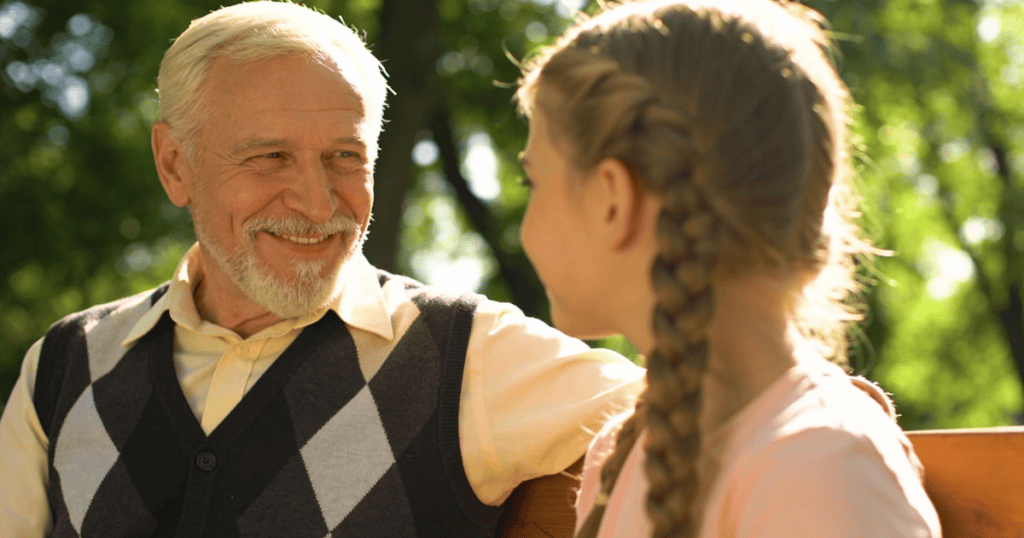 An older gentleman with a beard smiles gently at a young girl with braided hair outdoors, capturing a seemingly innocent interaction that masks the 10 things a narcissistic grandparent is teaching your children.