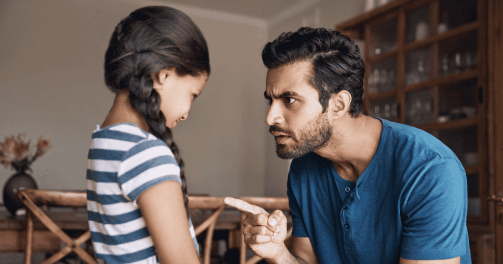 A father pointing accusingly at his young daughter while scolding her, illustrating how a narcissistic parent reacts with anger and control when their child begins to outgrow them intellectually.