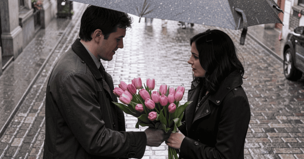 A man presents a large, vibrant bouquet of pink tulips to a woman on a wet cobblestone street under an umbrella, capturing the intense early stage of love bombing.