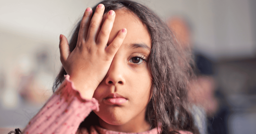 A young girl covering one eye with a guarded expression, symbolizing the unresolved childhood wounds and learned patterns of self-protection that can later make someone a target for narcissistic relationships.