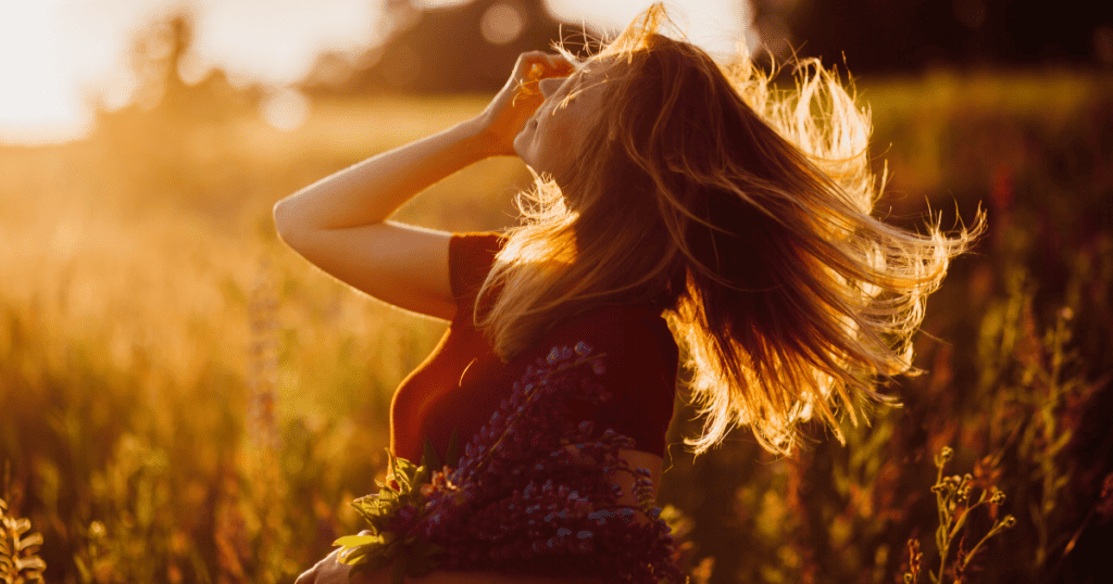 A woman freely tossing her hair in a sunlit field, radiating the untamed liberation of someone who has been pushed so far by a narcissist that she has grown beyond anyone's ability to control her.